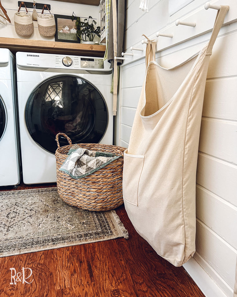 white wood wall with canvas laundry hamper hanging on white peg rail